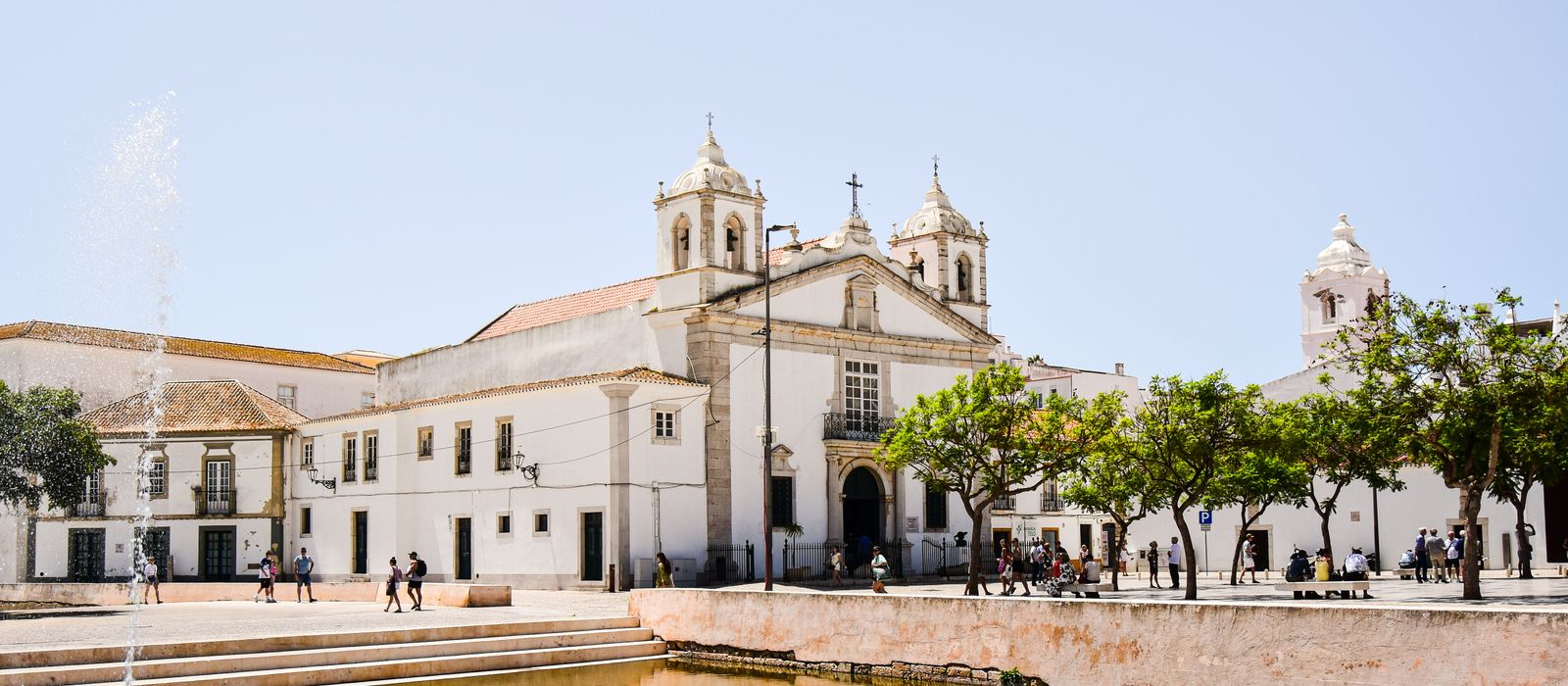 Scenic view of a historic church and lively square in Faro, Portugal, with a fountain and trees. — flights from Nantes to Faro
