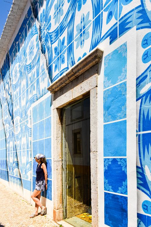Free A woman leaning against a vibrant blue azulejo-tiled wall in the sunny Faro District, Portugal. Stock Photo