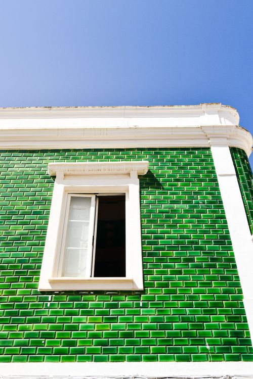Free A vibrant green tiled facade with an open window under a clear blue sky in Faro, Portugal. Stock Photo