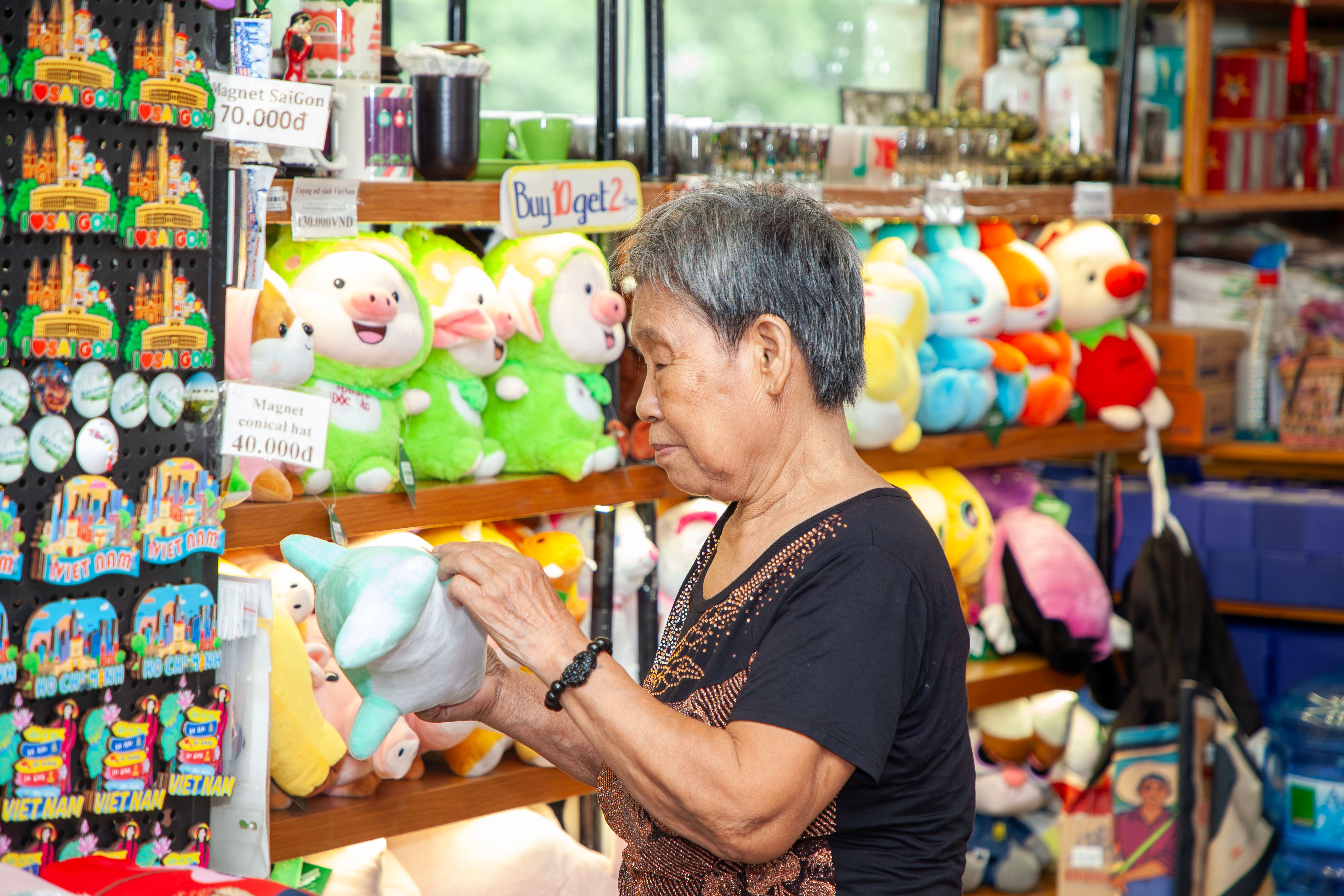 An elderly woman inspects stuffed toys in a vibrant Vietnamese souvenir shop.