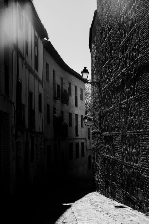 Free Black and white photo of a narrow alley in Toledo, Spain, with dramatic lighting and shadows. Stock Photo