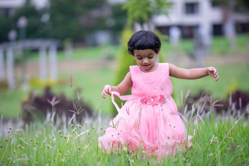 Free A young girl in a pink dress enjoying nature in a grassy outdoor setting, full of joy and exploration. Stock Photo