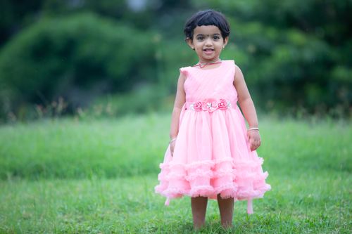 Free Charming young child wearing a pink dress smiling outdoors, captured beautifully in natural light. Stock Photo
