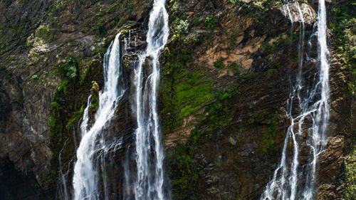 Free A stunning waterfall flows over a moss-covered rocky cliff surrounded by lush greenery. Stock Photo