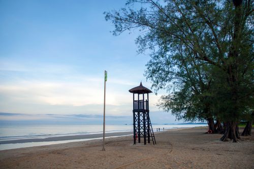 Free Serene beach at sunrise with a lifeguard tower and lush trees. Stock Photo