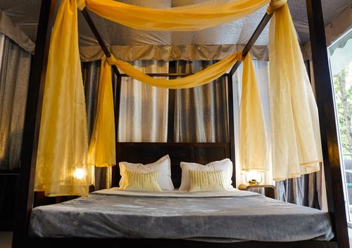 Free Elegant four poster bed with flowing yellow curtains in a cozy, serene bedroom setting. Stock Photo