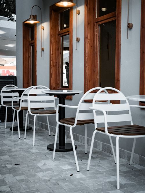 Free Stylish outdoor cafe setting with white chairs and wooden decor, perfect for relaxed dining. Stock Photo