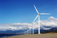 晴朗的蓝天下，沙质海岸线上安装了一排风力涡轮机，促进了可再生能源