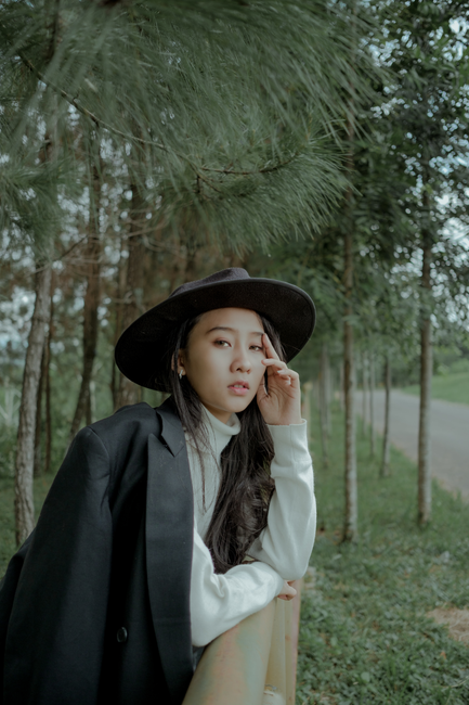 A young woman in the forest wearing a black hat and coat in a serene outdoor setting.