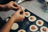 Hands folding dumplings on a tray with meat filling, showcasing traditional food preparation.