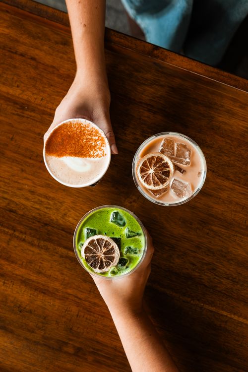 Free Three diverse drinks with cinnamon, citrus, and matcha on a wooden table, captured from above. Stock Photo