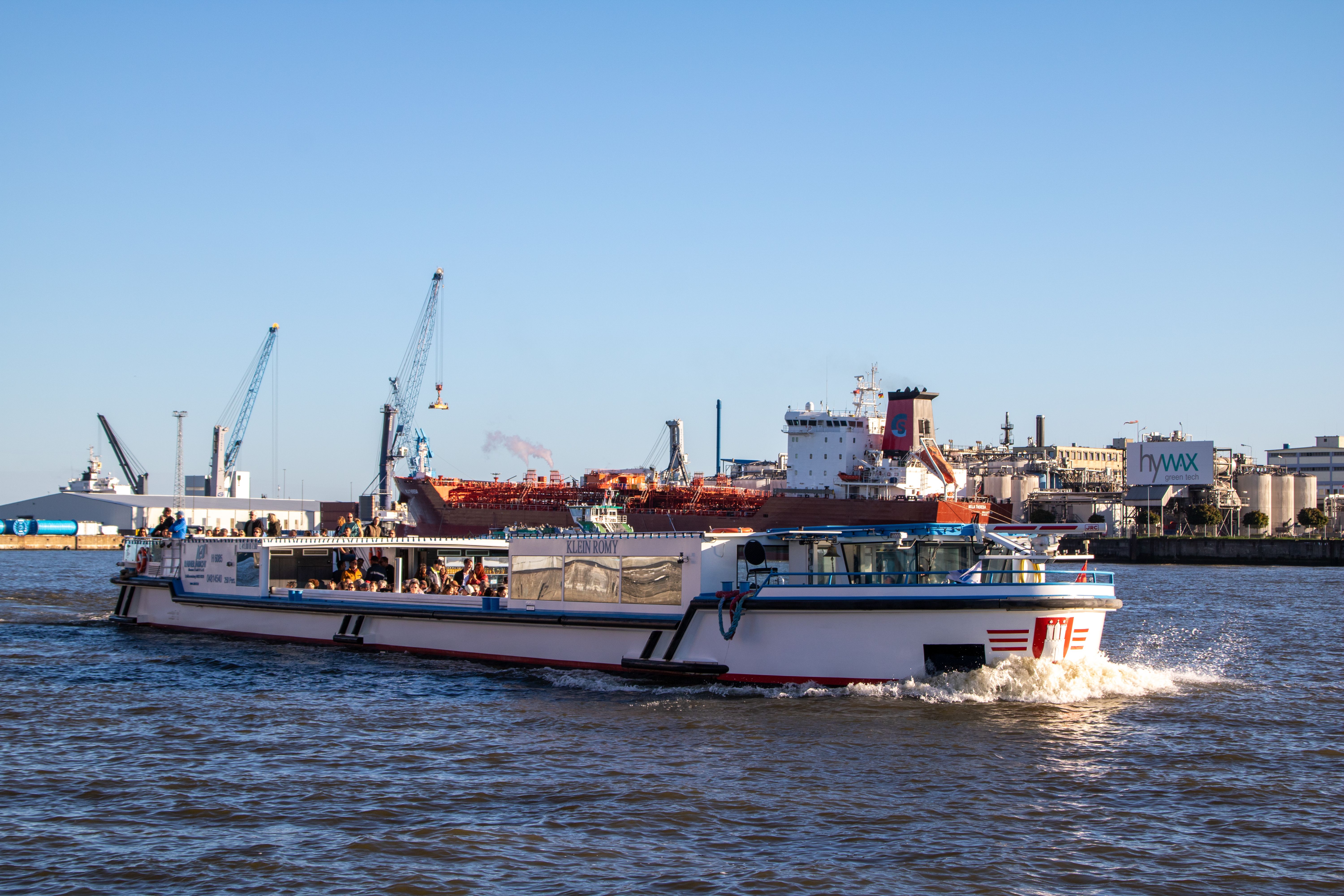 Tourist boat cruising through the bustling Hamburg port on a sunny day.