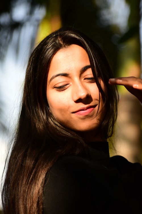 Free A candid outdoor portrait of a smiling woman basking in sunlight with a serene background. Stock Photo