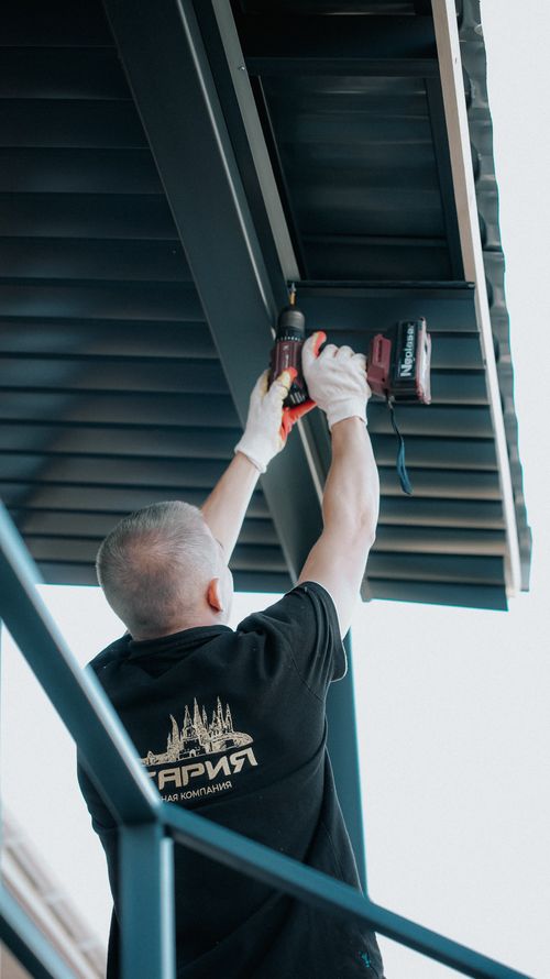 Free A construction worker uses a drill to install a metal roof on a building, showcasing modern architecture techniques. Stock Photo
