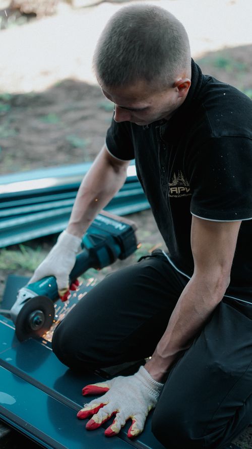 Free Man cutting metal with an angle grinder outdoors, showing sparks flying, wearing protective gloves. Stock Photo