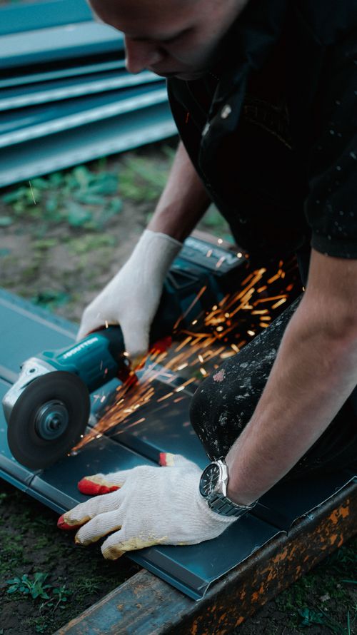 Free A worker in gloves uses an angle grinder on metal outdoors, producing bright sparks. Stock Photo