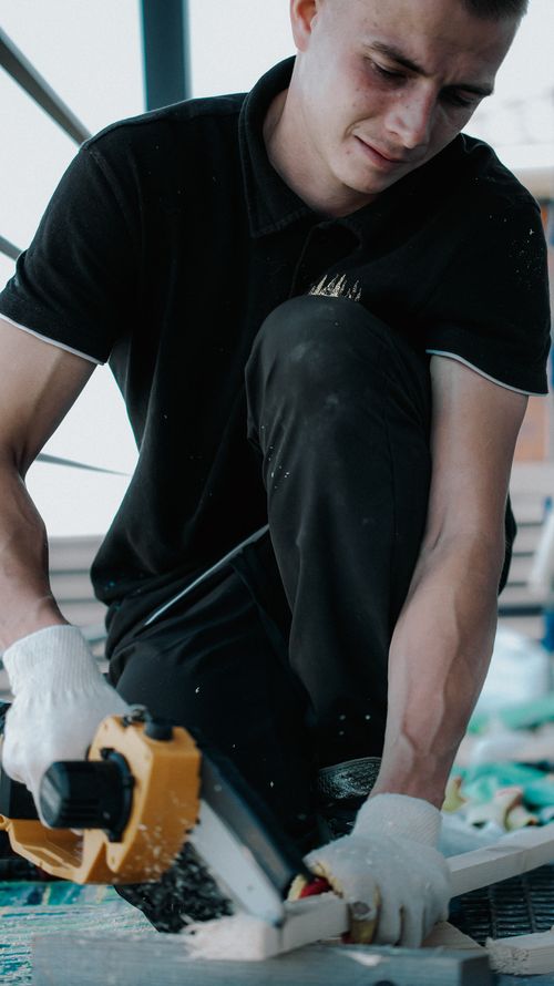 Free Focused young carpenter cutting wood with precision outdoors. Stock Photo