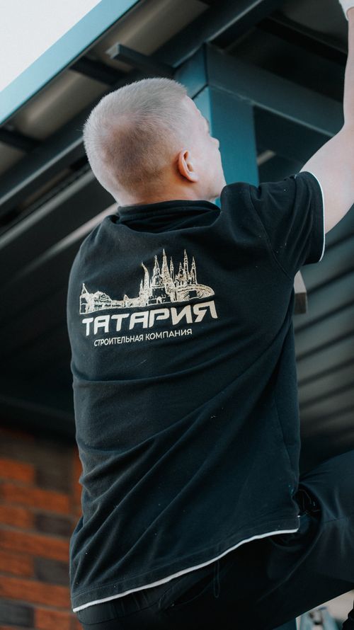 Free Man in black shirt with company logo climbing on industrial metal structure outdoors. Stock Photo