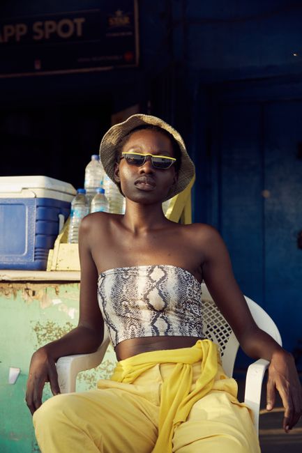 Chic African woman in sunglasses and snake print top, Accra street fashion scene.