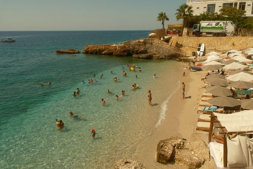 Free Relaxing beach scene in Vlorë, Albania with turquoise water, sunbathers, and umbrellas under the summer sun. Stock Photo