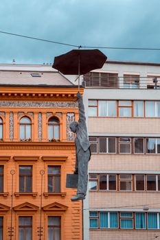 Unique sculpture of a man with an umbrella hanging mid-air amidst urban buildings.