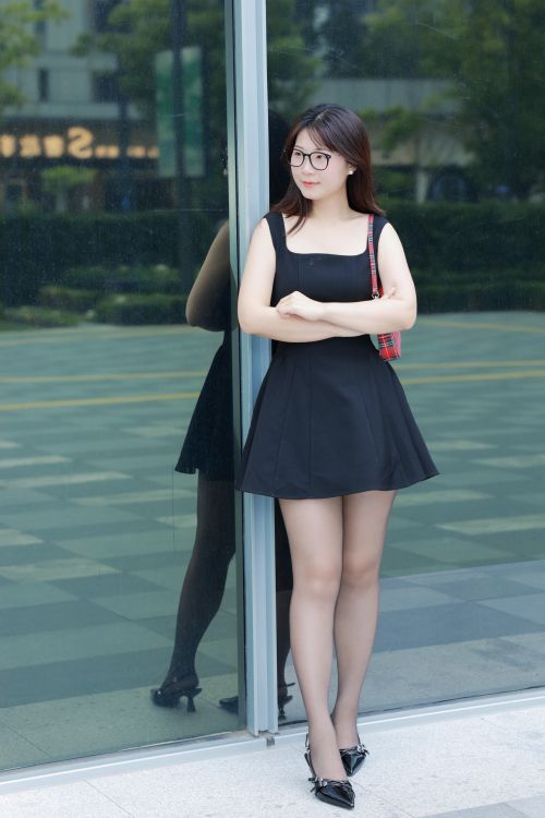 Free Modern young woman in a black dress stands confidently by a glass wall in Hefei, China. Stock Photo