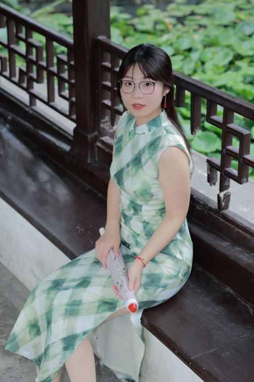 Free A young woman in a traditional green and white dress sits in a serene garden setting in Hefei, China. Stock Photo