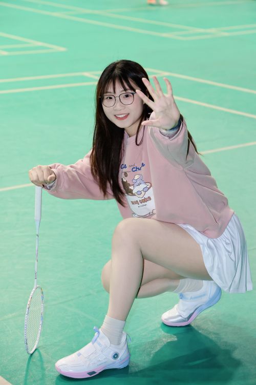 Free Smiling young woman in casual sportswear poses with a badminton racket on an indoor court. Stock Photo