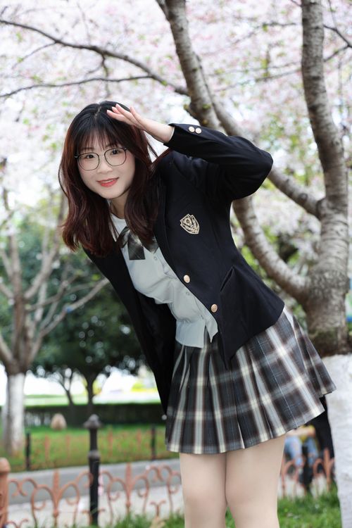 Free Young woman in school uniform enjoys cherry blossoms in a sunny Hefei park. Stock Photo