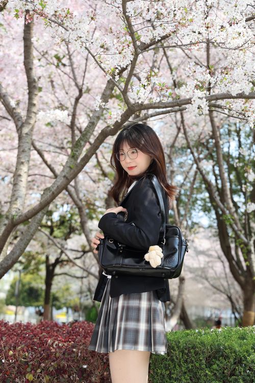 Free Young woman posing under cherry blossoms in Hefei, China, wearing a plaid skirt and glasses. Stock Photo
