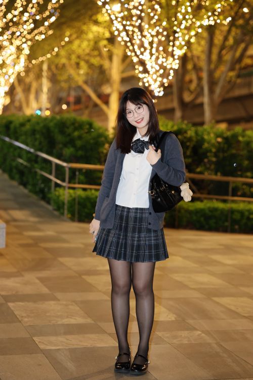 Free A young woman stands outdoors at night, elegantly dressed in a school outfit with lights in the background. Stock Photo