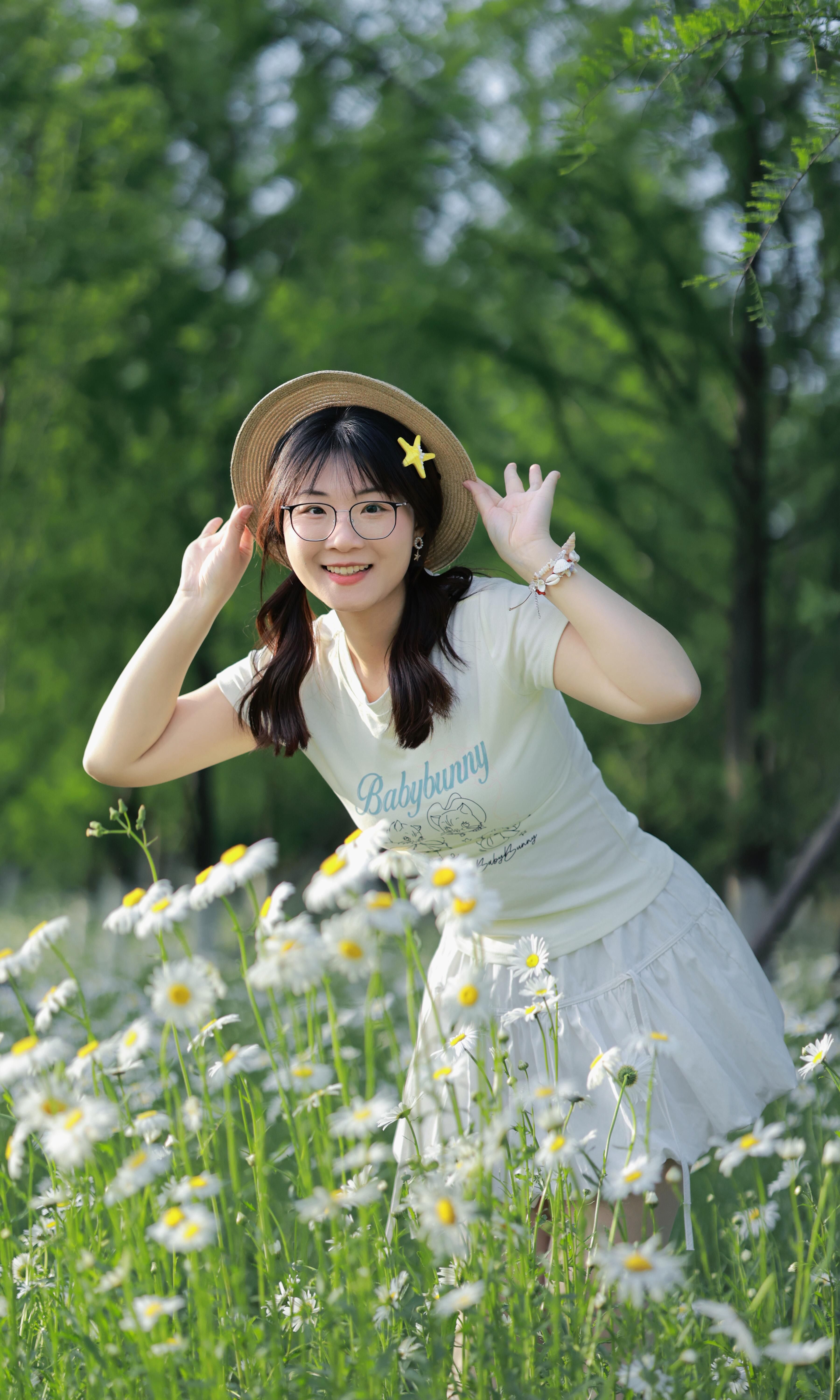 Smiling woman with hat and glasses in a daisy field during spring.