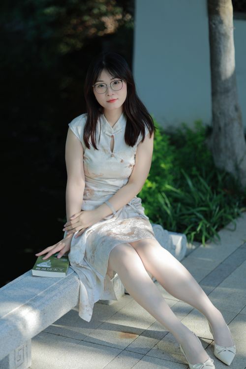 Free Portrait of a young woman in a traditional Chinese dress sitting outdoors on a sunny day. Stock Photo