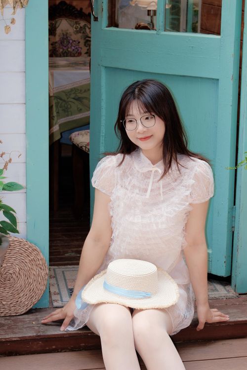 Free Young woman sitting by a turquoise door holding a straw hat in Hefei, China. Stock Photo