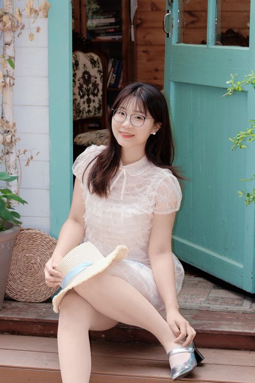 Free Young woman in a summer dress sitting by a vibrant turquoise door in Hefei, China. Stock Photo
