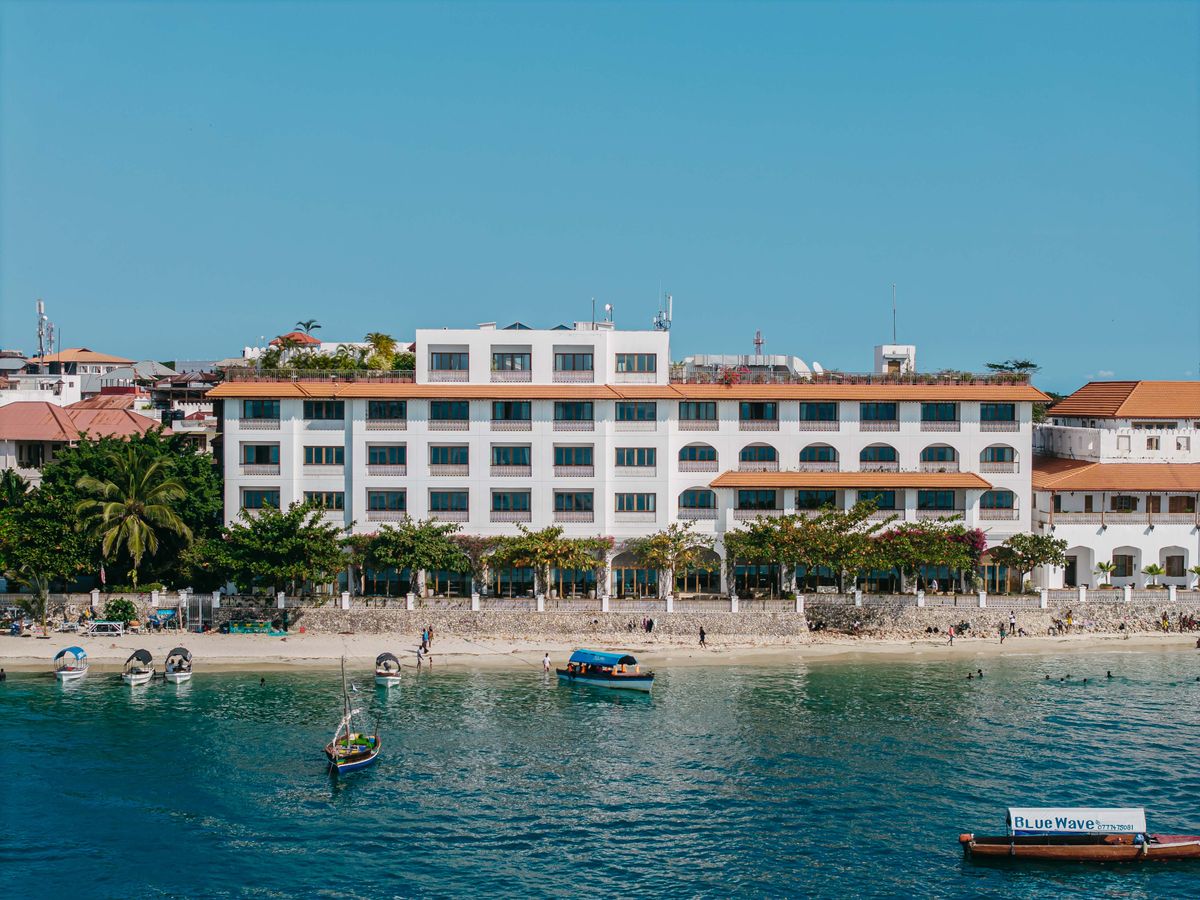 Elegant beachfront hotel in vibrant Stone Town, Zanzibar, with clear blue skies and boats.