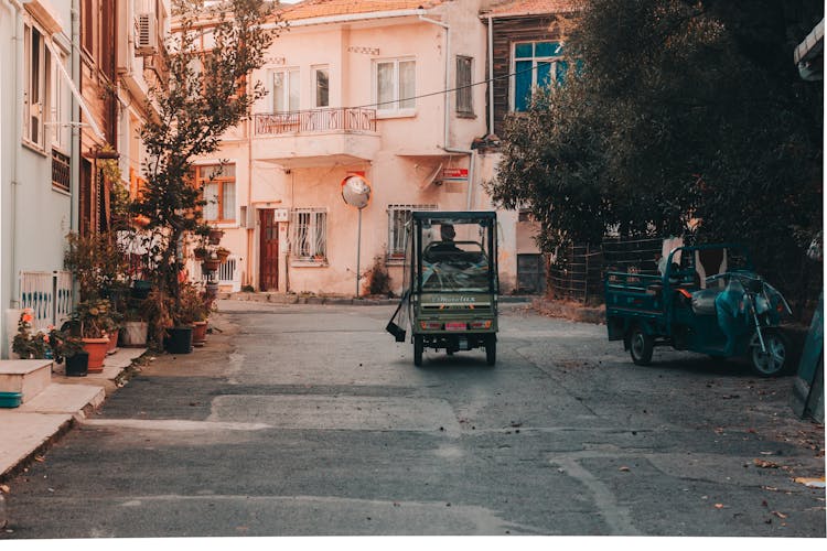 A Person Driving A Vehicle On A Road Between Houses