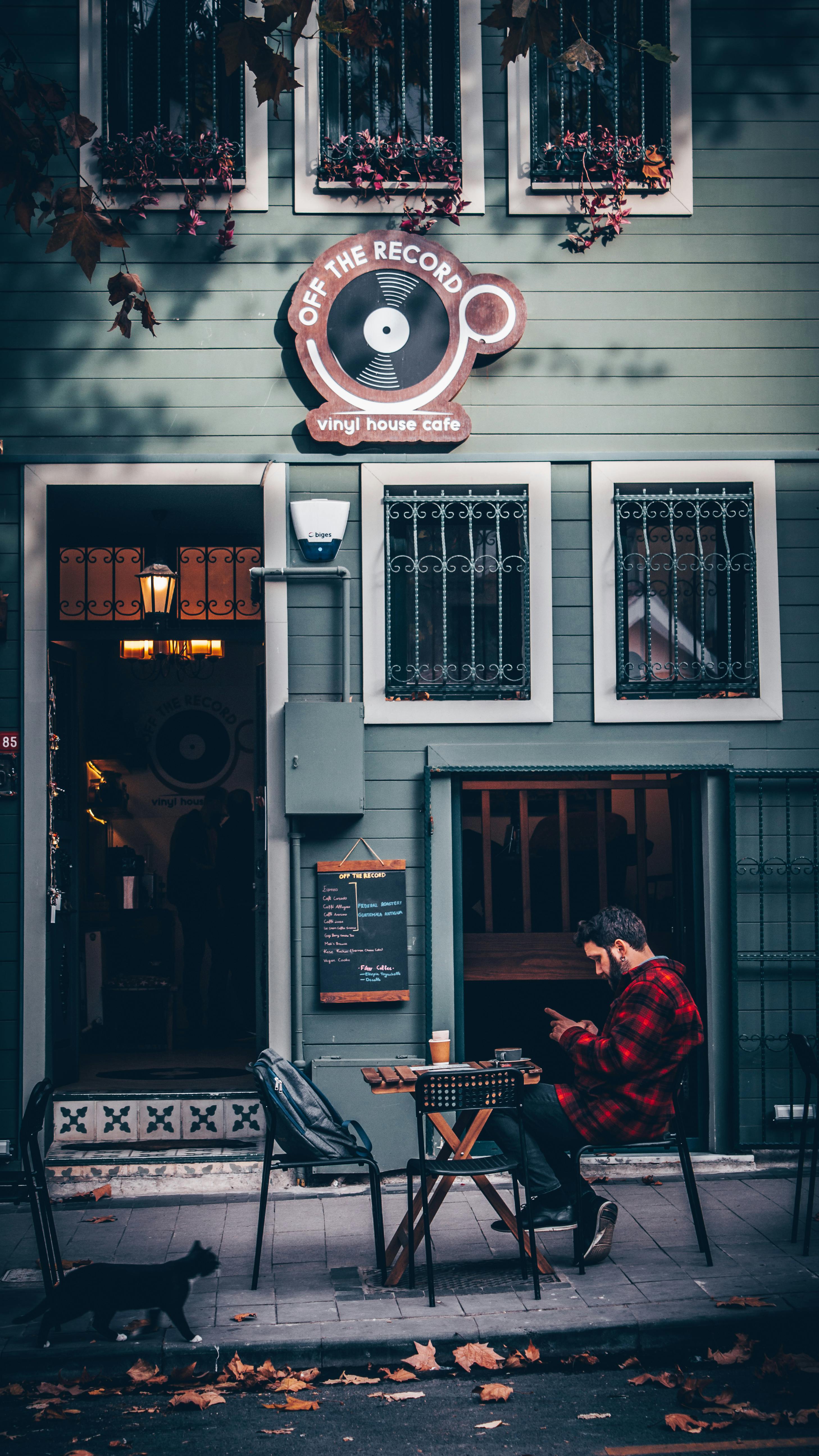 a man wearing a plaid shirt using his smartphone while sitting outside of a cafe