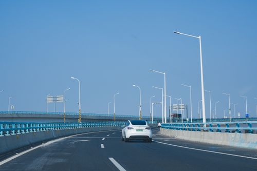 Free A white car travels on a long highway bridge under a clear blue sky, conveying a sense of freedom and travel. Stock Photo