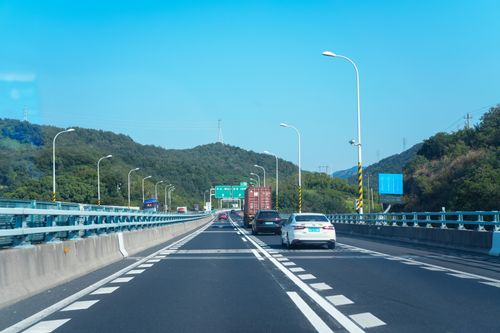Free Vehicles on a highway through lush mountains under a clear blue sky. Stock Photo