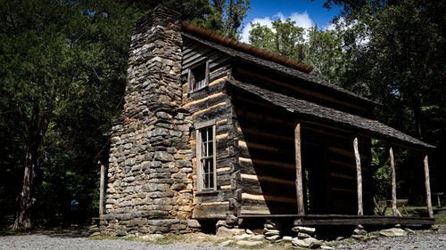 Free Historic log cabin with stone chimney located in a lush forested area. Stock Photo