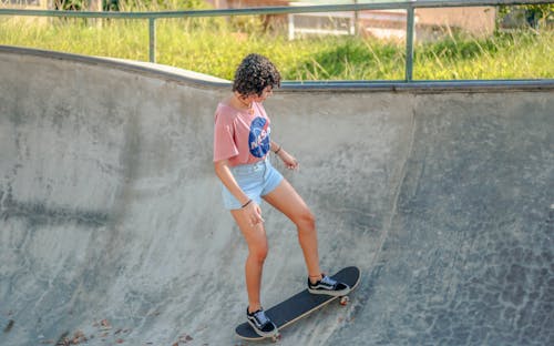 Free Woman In Pink Shirt And Denim Shorts Skating Stock Photo