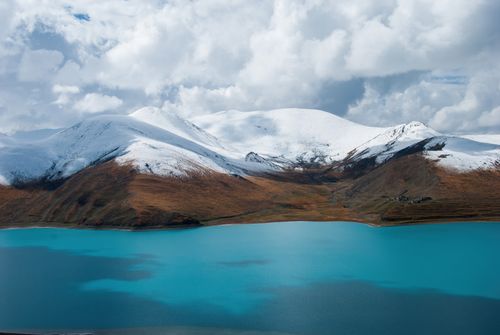 Free Breathtaking snowy mountains overlooking a vibrant turquoise lake under cloudy skies. Stock Photo