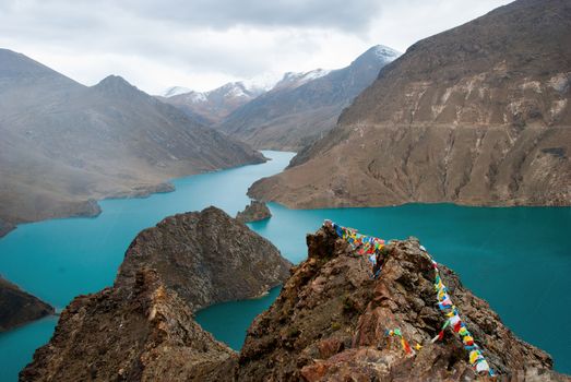 A breathtaking view of a turquoise mountain lake in the Himalayas, adorned with colorful prayer flags.