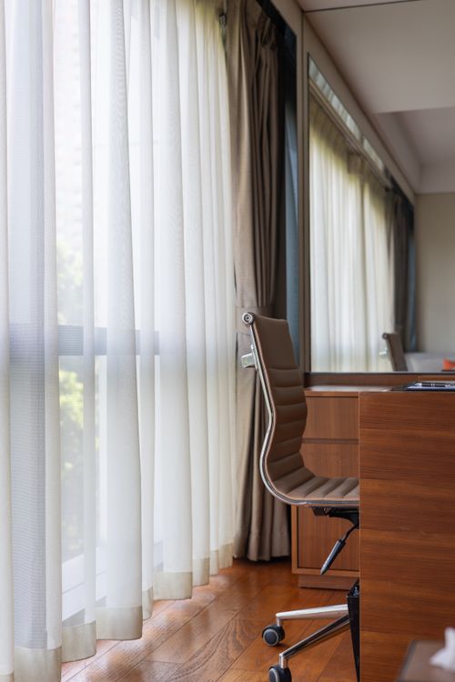 Free Comfortable office chair by a sunlit window with sheer curtains, creating a serene workspace vibe. Stock Photo