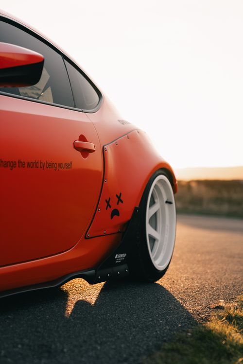 Free Close-up of a modified red sports car with custom wheels at sunset creates a vibrant scene. Stock Photo