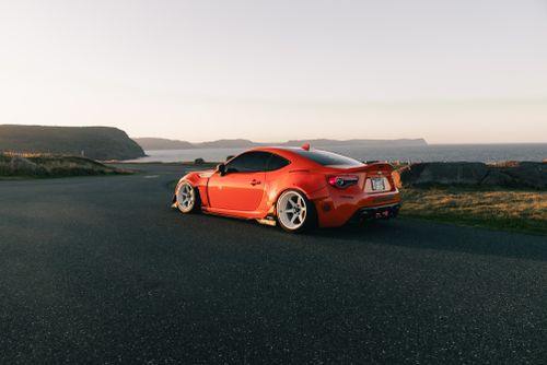 Free Red sports car parked by a scenic ocean view during sunset, showcasing sleek design and vibrant color. Stock Photo