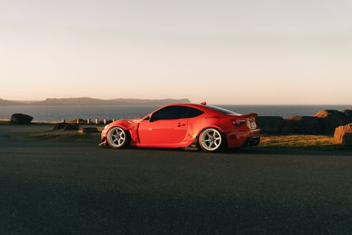 Free A sleek red sports car parked by an oceanfront during a serene sunset, capturing elegance and adventure. Stock Photo