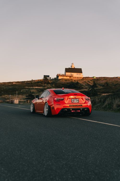 Free A sleek red sports car drives on a scenic road at dusk near a hilltop building. Stock Photo