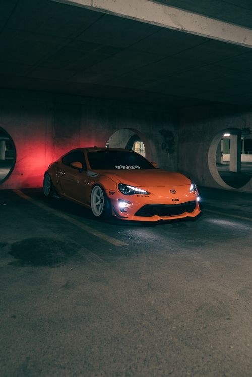 Free Bright orange sports car parked in a dimly lit urban environment, featuring sleek design and modern aesthetics. Stock Photo